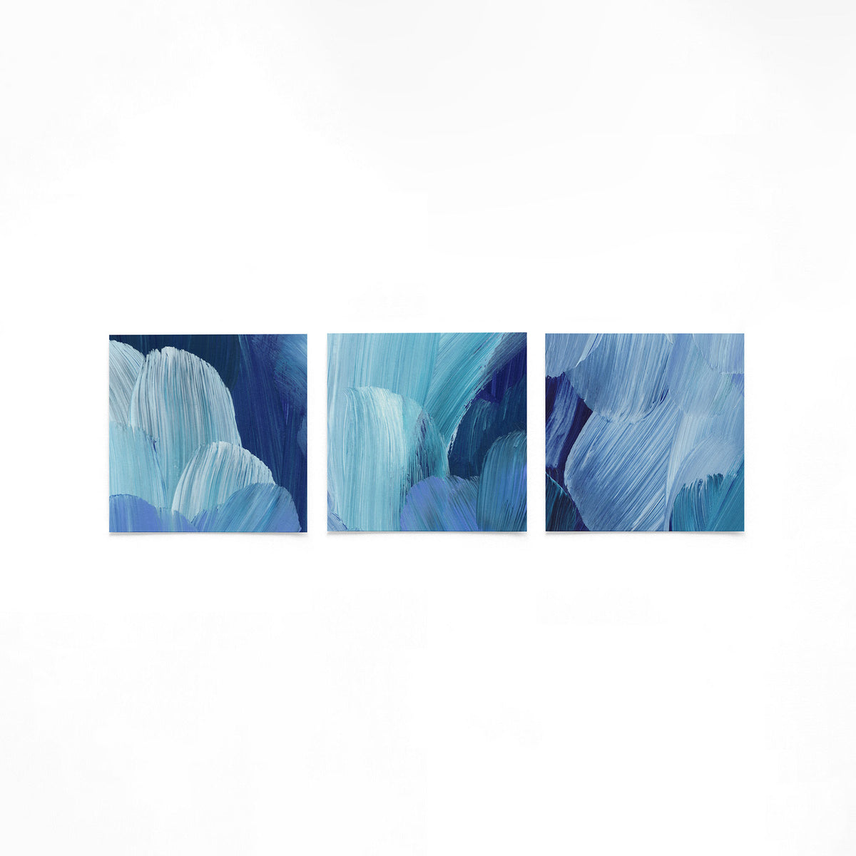 Drie vierkante posters met blauwe penseelstreken op een gebroken witte achtergrond
